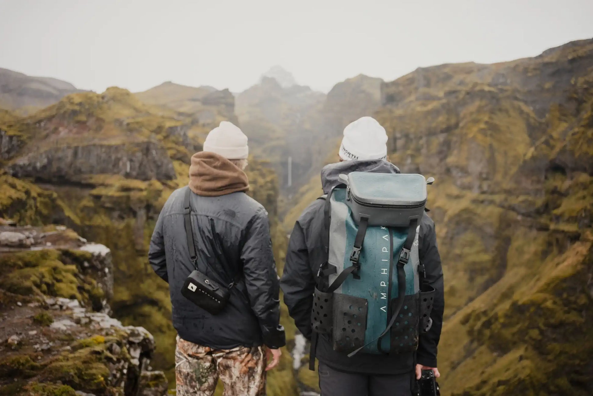 beautiful iceland landscape mountains and green cliffs rolling hills with black rock and two people standing with sko gear crossbody and karpathos waterproof backpack