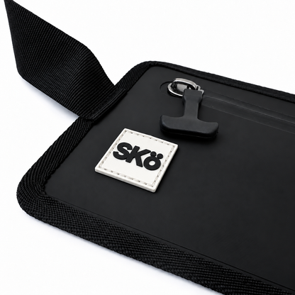 Phone Pouch in Matte Black, close-up of white square SKÖ logo patch, waterproof zipper pull and woven black trim.